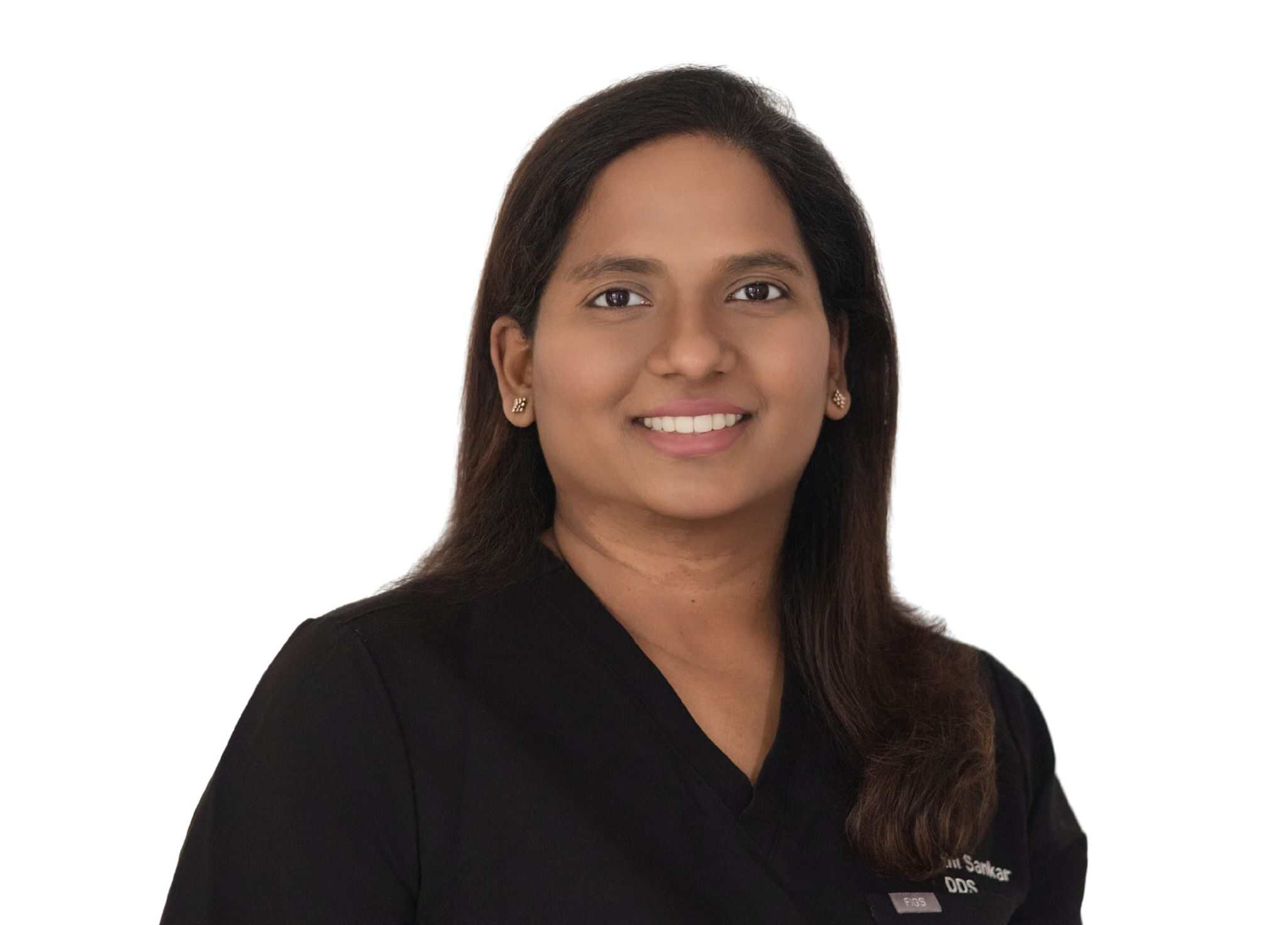 Professional headshot of a smiling woman in black scrubs against a white background, facing the camera.